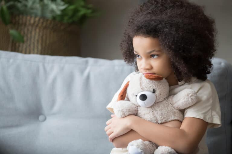 Girl holding teddy bear looking away